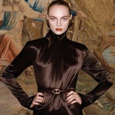 Model with her hands on her hips wearing a mock neck brown satin dress sold at Net-A-Porter