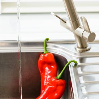 Red peppers rinsed under water in kitchen sink