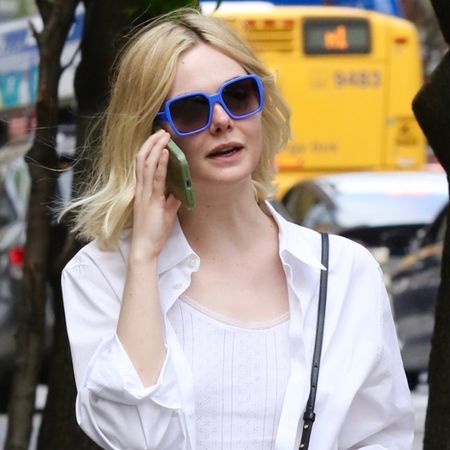 Elle Fanning walking in NYC wearing a white shirt, dark-wash cuffed jeans, a crossbody Bottega Veneta bag, and red Miu Miu rope sandals.