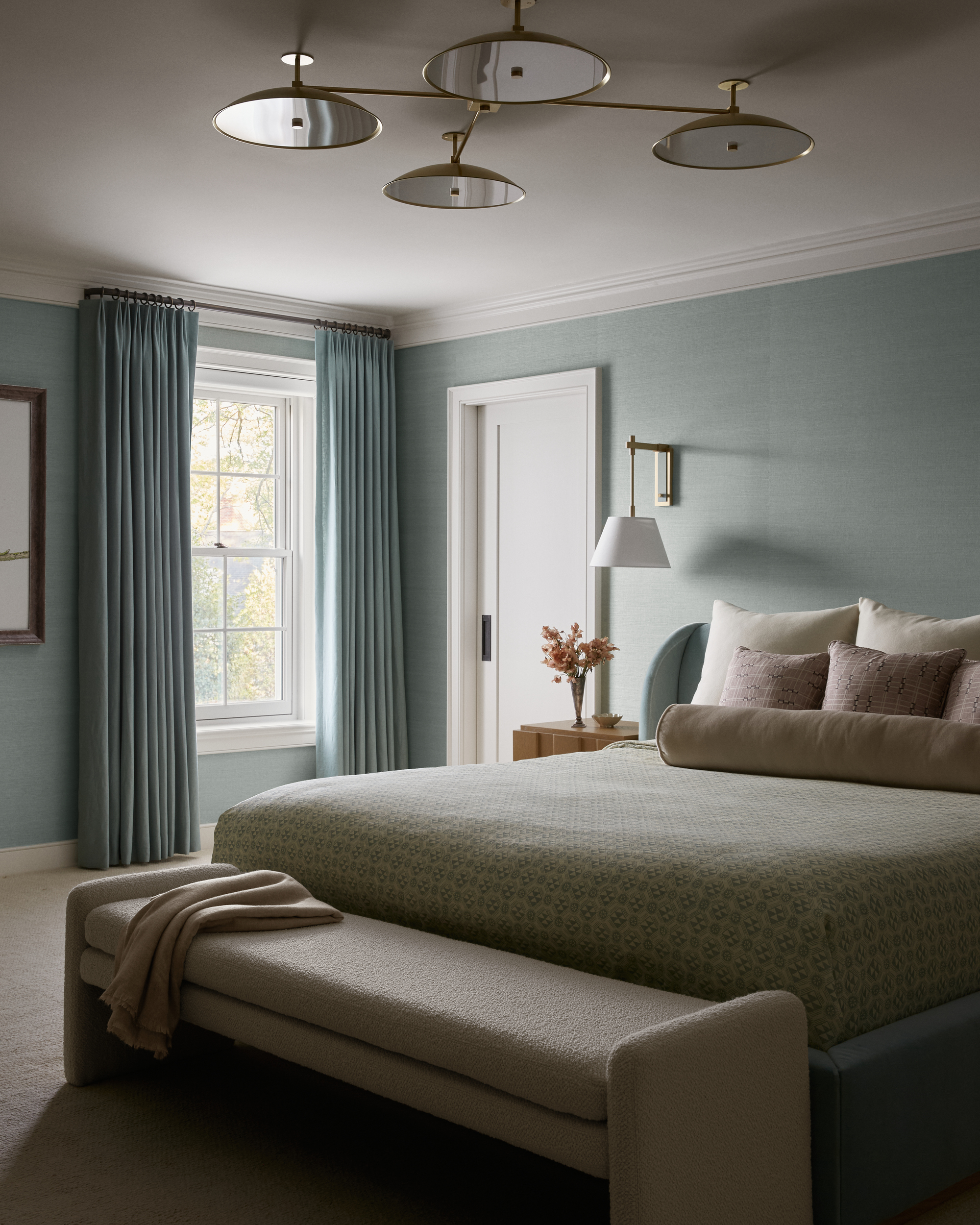 modern bedroom with light blue walls, blue curtains, bed with cushions, and bench seat at the end of the bed