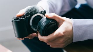 Photographer taking the lens off a Sony ZV-E10 camera