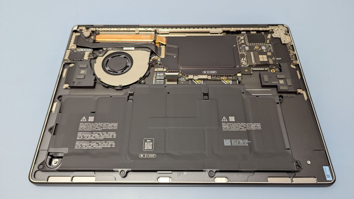 Microsoft Surface Laptop 7 15 upside down on table with underside cover removed, showing internals such as the battery, cooling system and SSD.