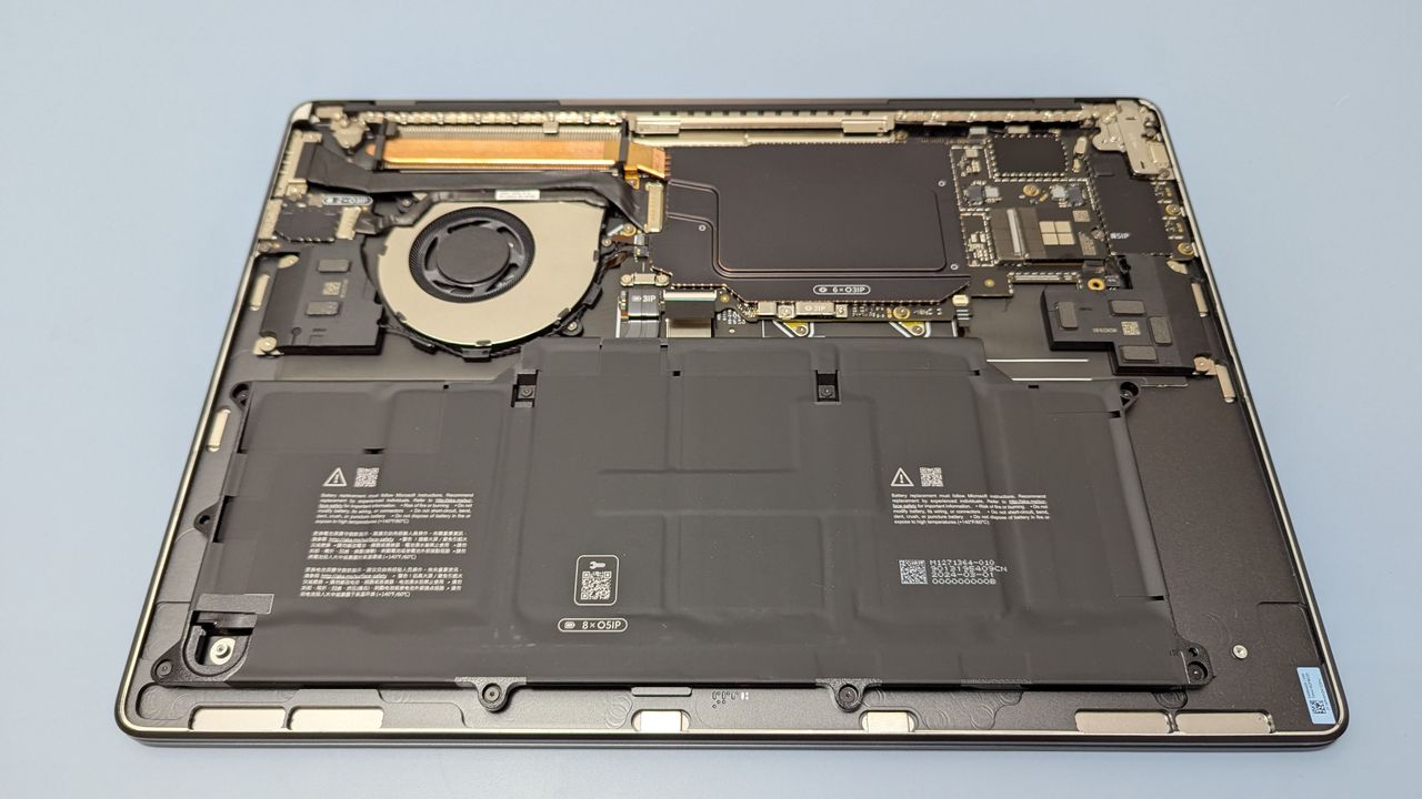 Microsoft Surface Laptop 7 15 upside down on table with underside cover removed, showing internals such as the battery, cooling system and SSD.
