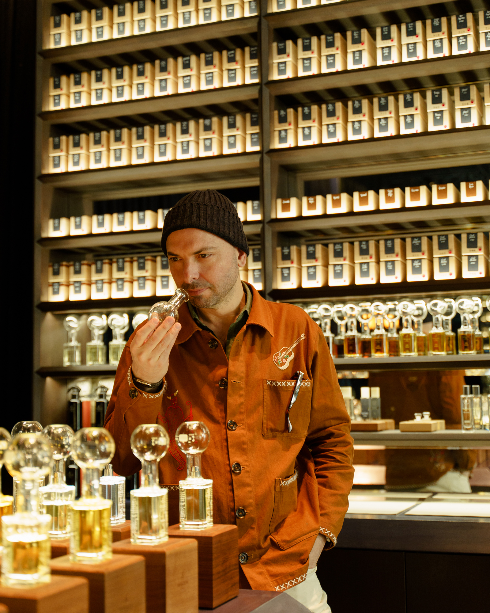 Julian Bedel in an orange coat surrounded by glass perfume bottles