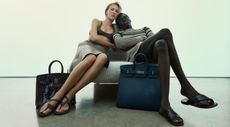 Male and female model sat on chair with two Hermès travel bags 