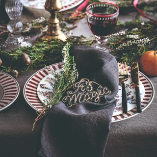 A dining table set for Christmas dinner with a black tablecloth and loosely draped black napkin on top of the plate