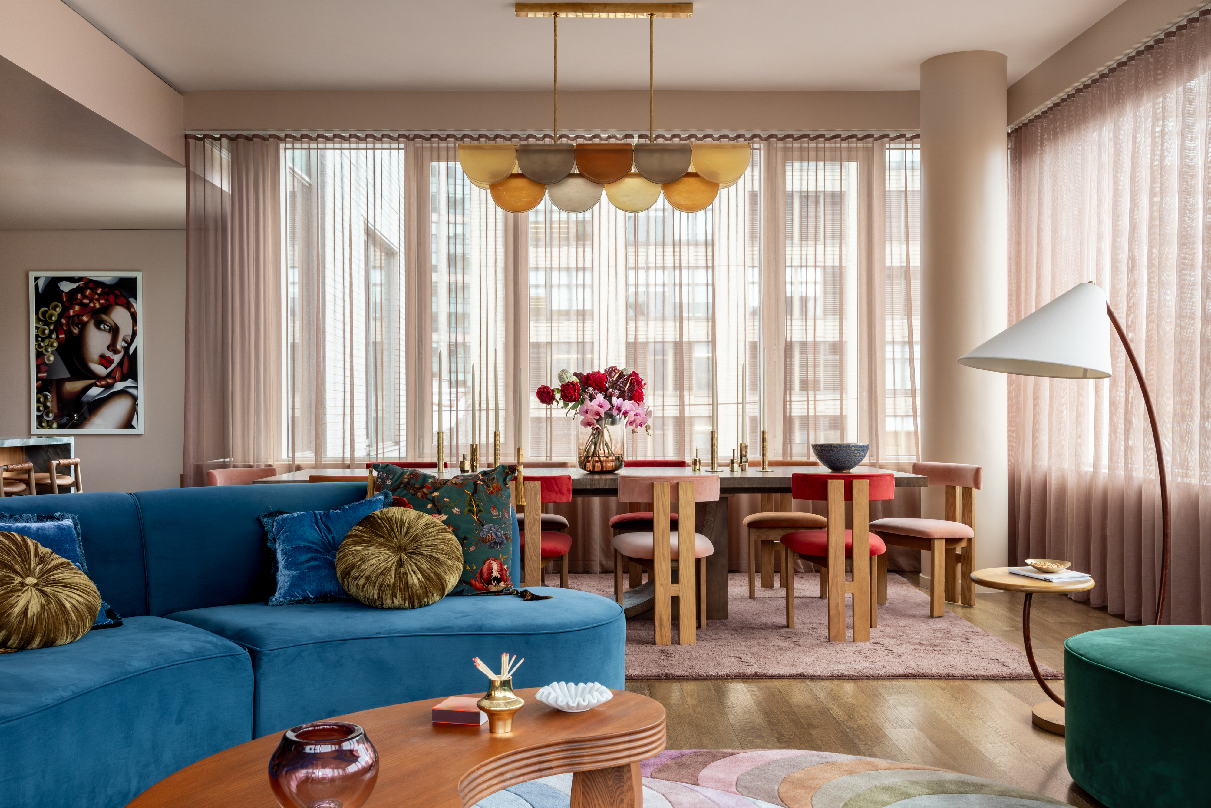 A living room cum dining, with a curving blue sofa, a white floor lamp and a curving coffee table