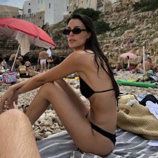 Leia Sfez wearing a black bikini and sunglasses on a European beach