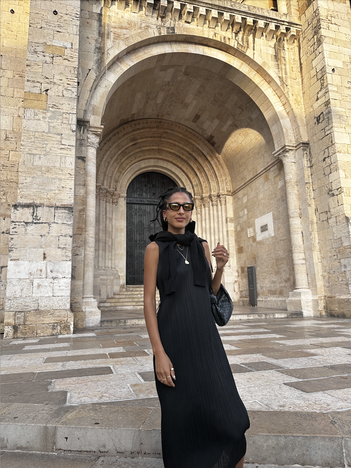 Madison Utendahl wearing sunglasses, black sweater over shoulders, and black dress standing in front of cathedral