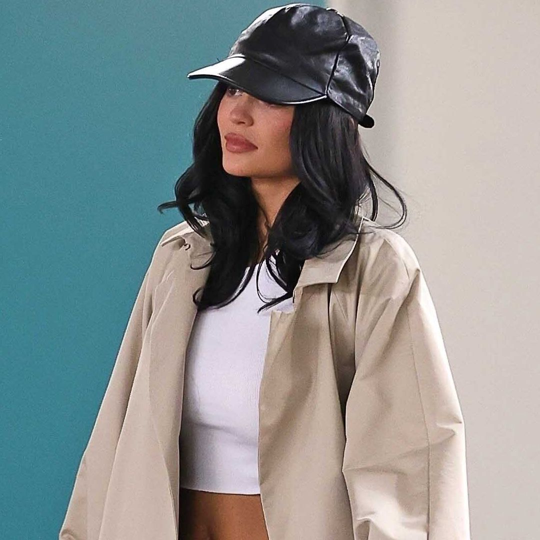 Kylie Jenner wore a trench coat with dark-wash indigo jeans, heeled flip-flops, and a leather baseball cap