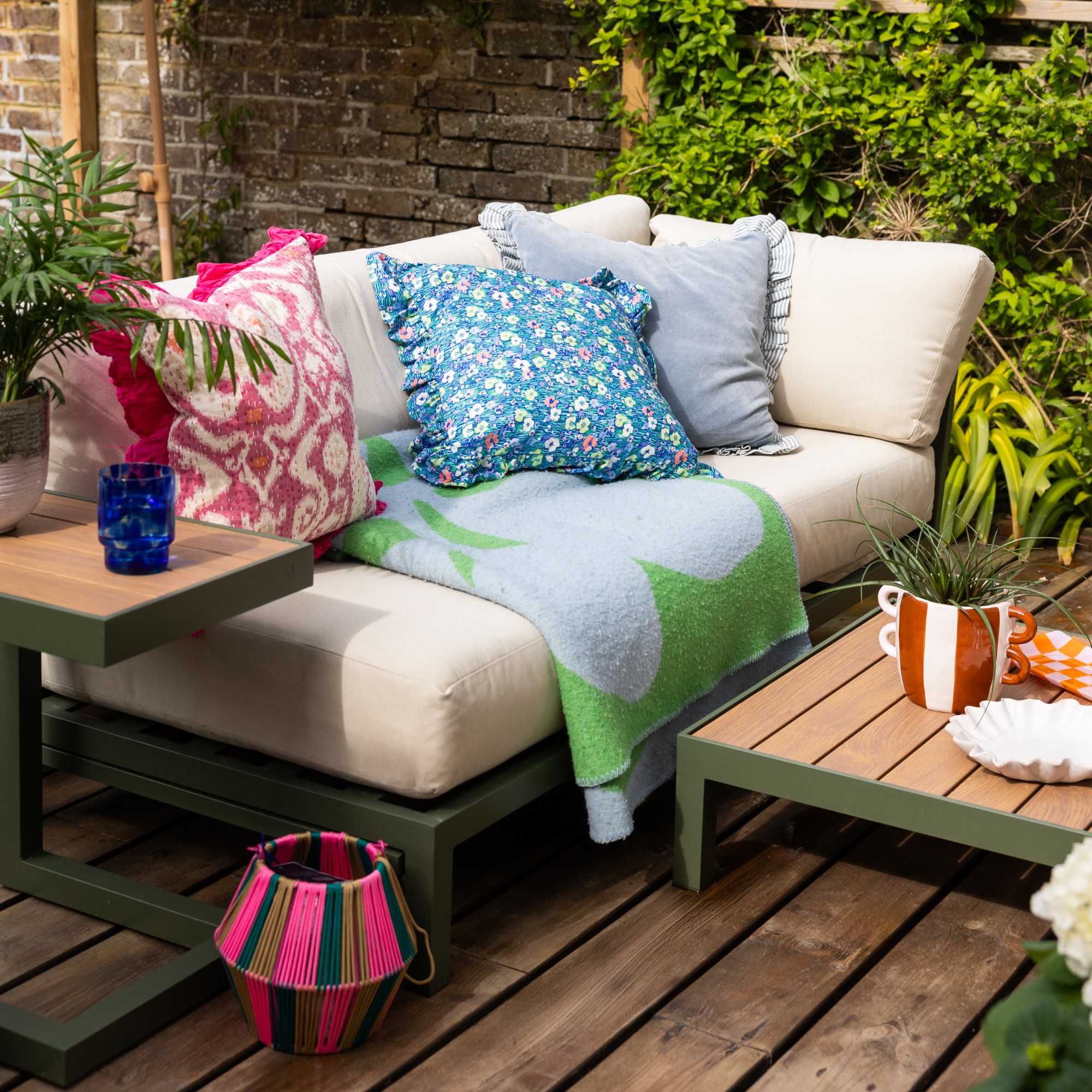 A garden with an outdoor sofa with a green metal frame and cream cushions and matching coffee and side tables