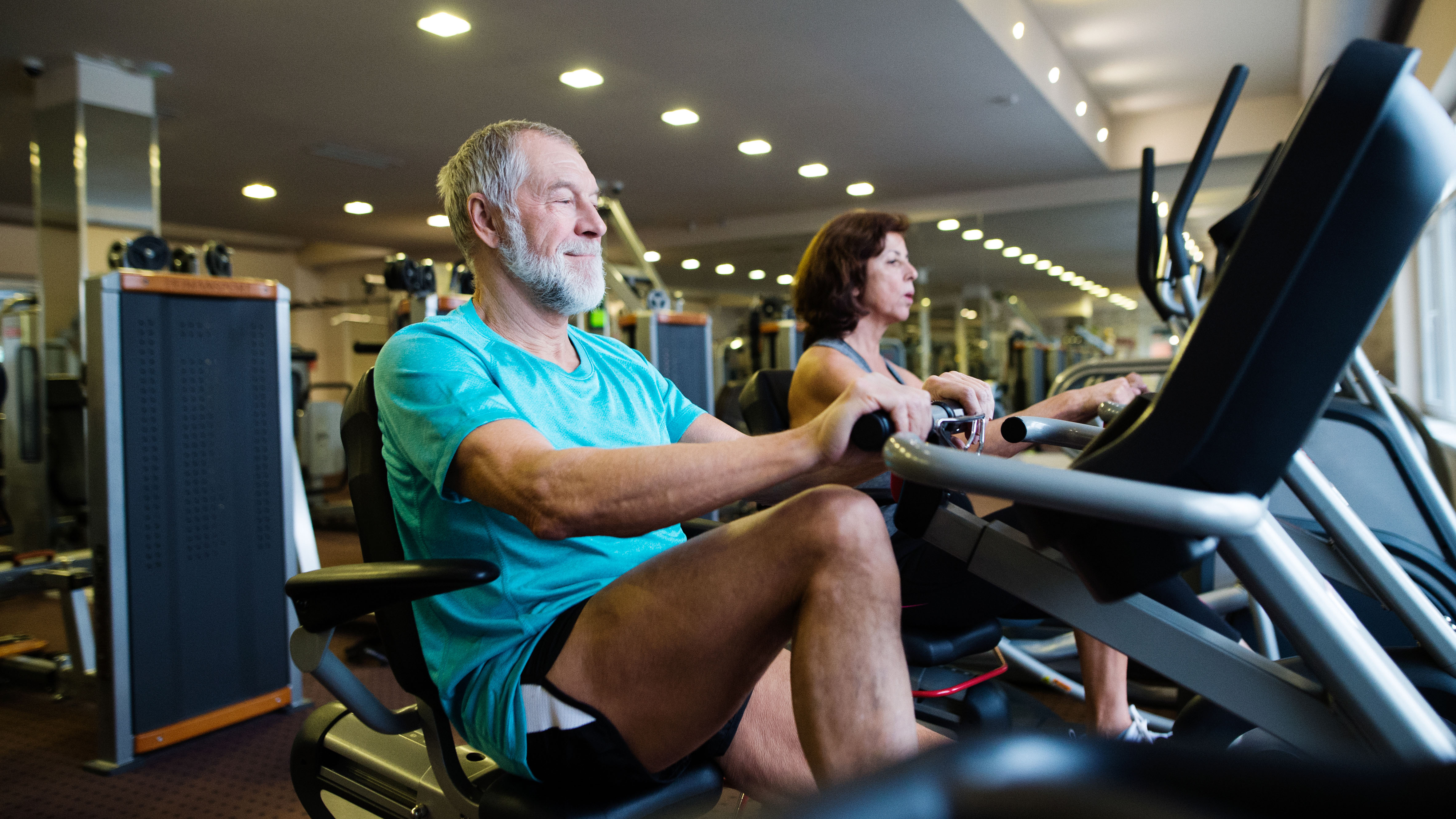 Older couple working out on recumbent exercise bikes in gym