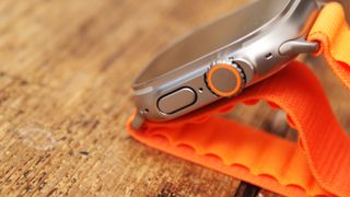 Apple Watch Ultra liggende på et bord med oransje rem.
