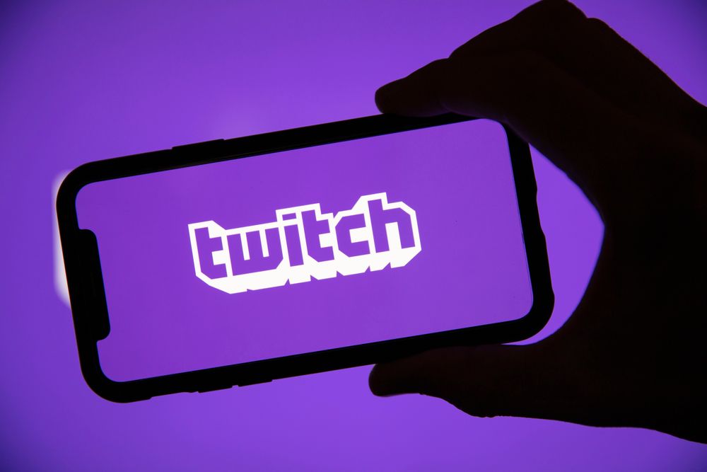 The Twitch logo on a smartphone being held by a shadowy hand