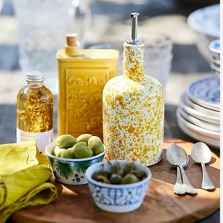 A white and yellow speckled olive oil bottle on an outdoor table spread