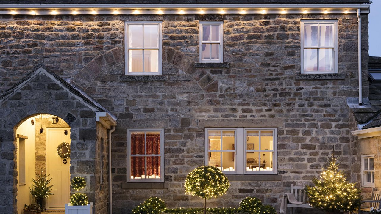 A home exterior with multiple sources of Christmas lighting decor including lit wreaths and fairy lights