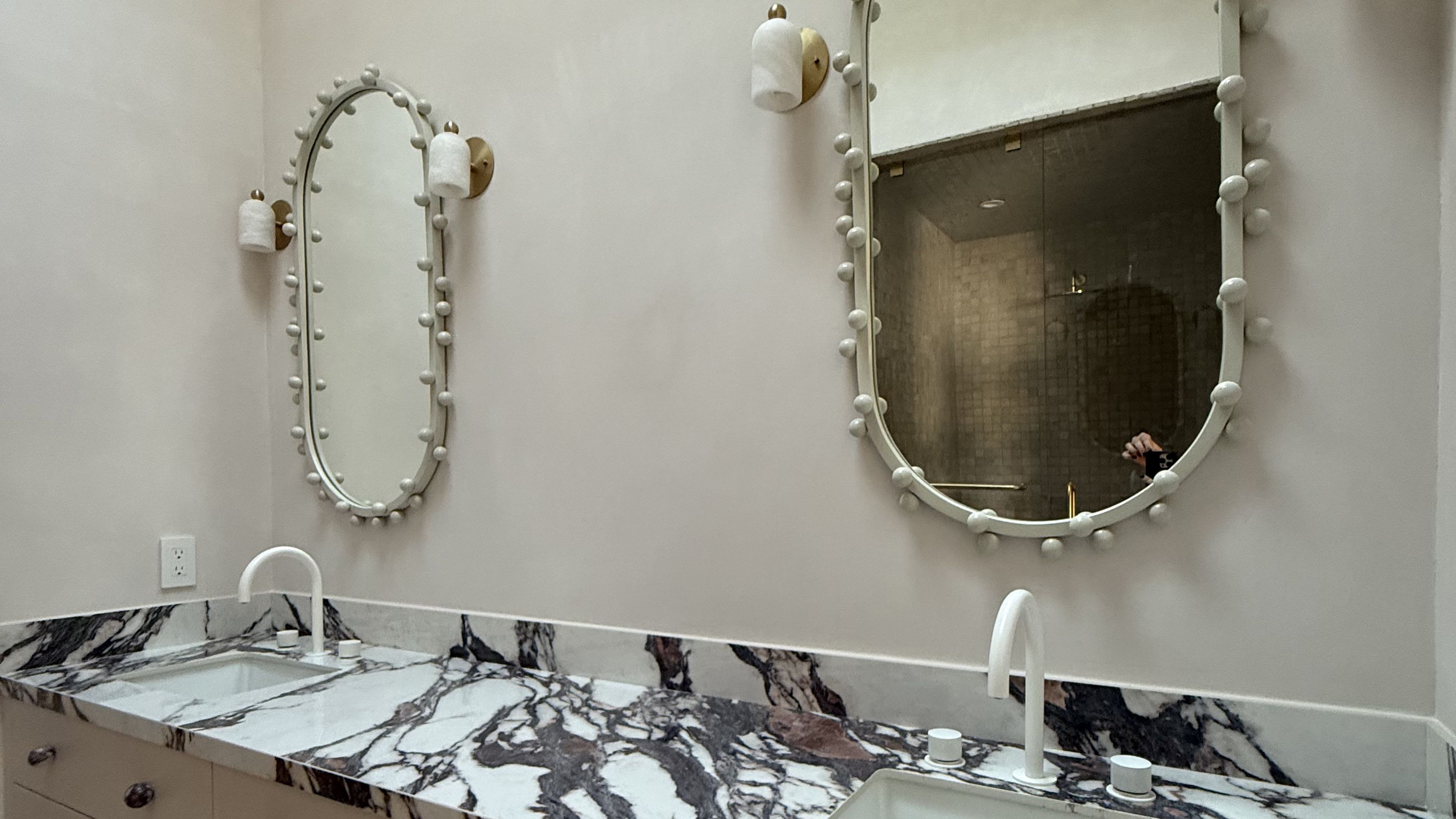 marble-topped bathroom vanity with two oval mirrors on the wall above it