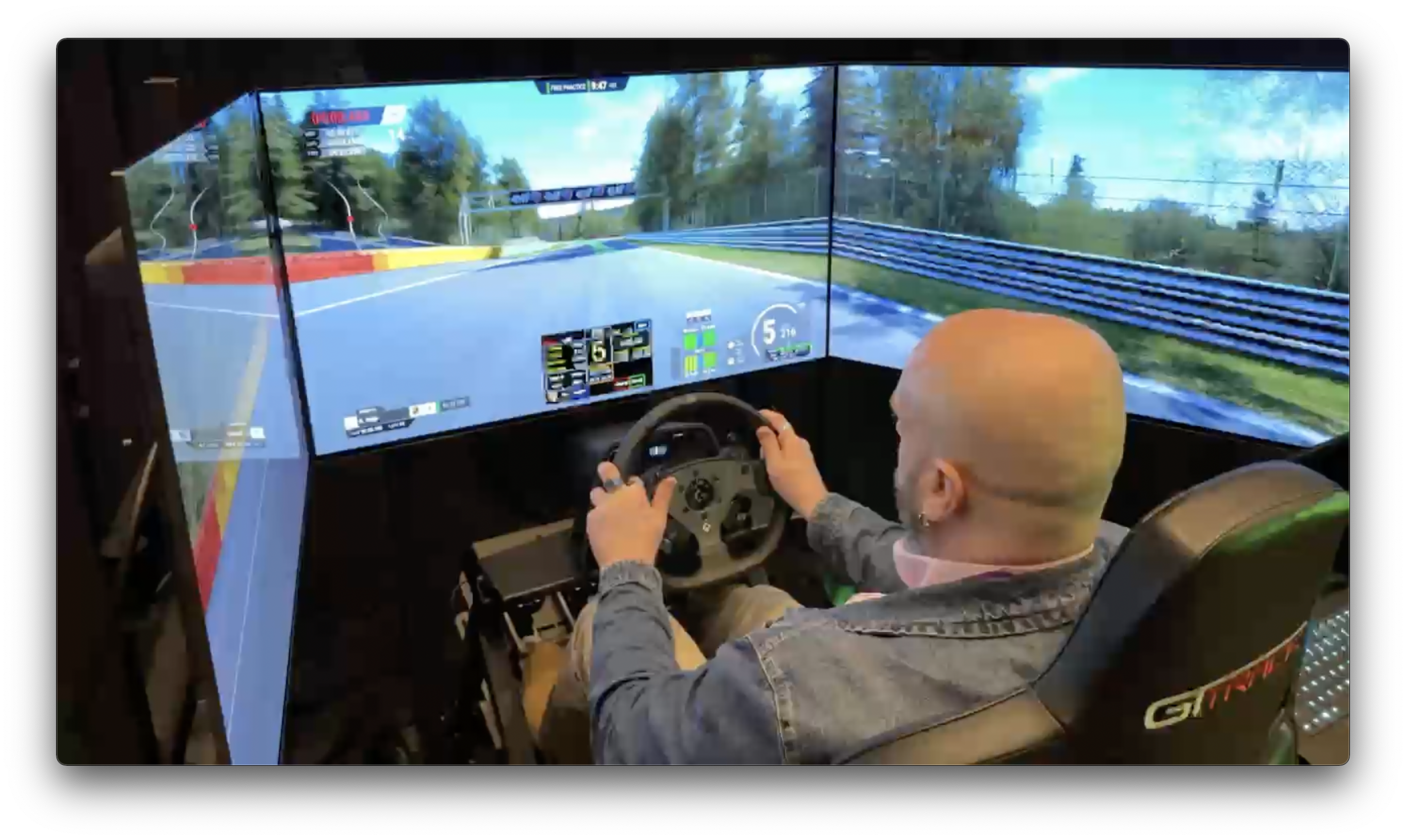 En man sitter och kör en racingsimulator med en ratt och tre skärmar runtom sig.