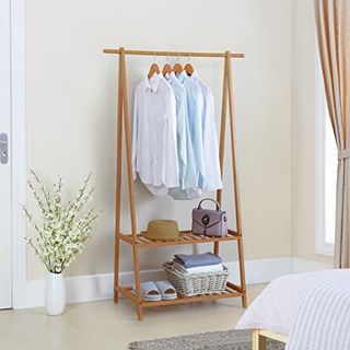 A wooden clothes hanging rack with some shirts hangign from it on wooden hangars. Two shelves below with baskets on 