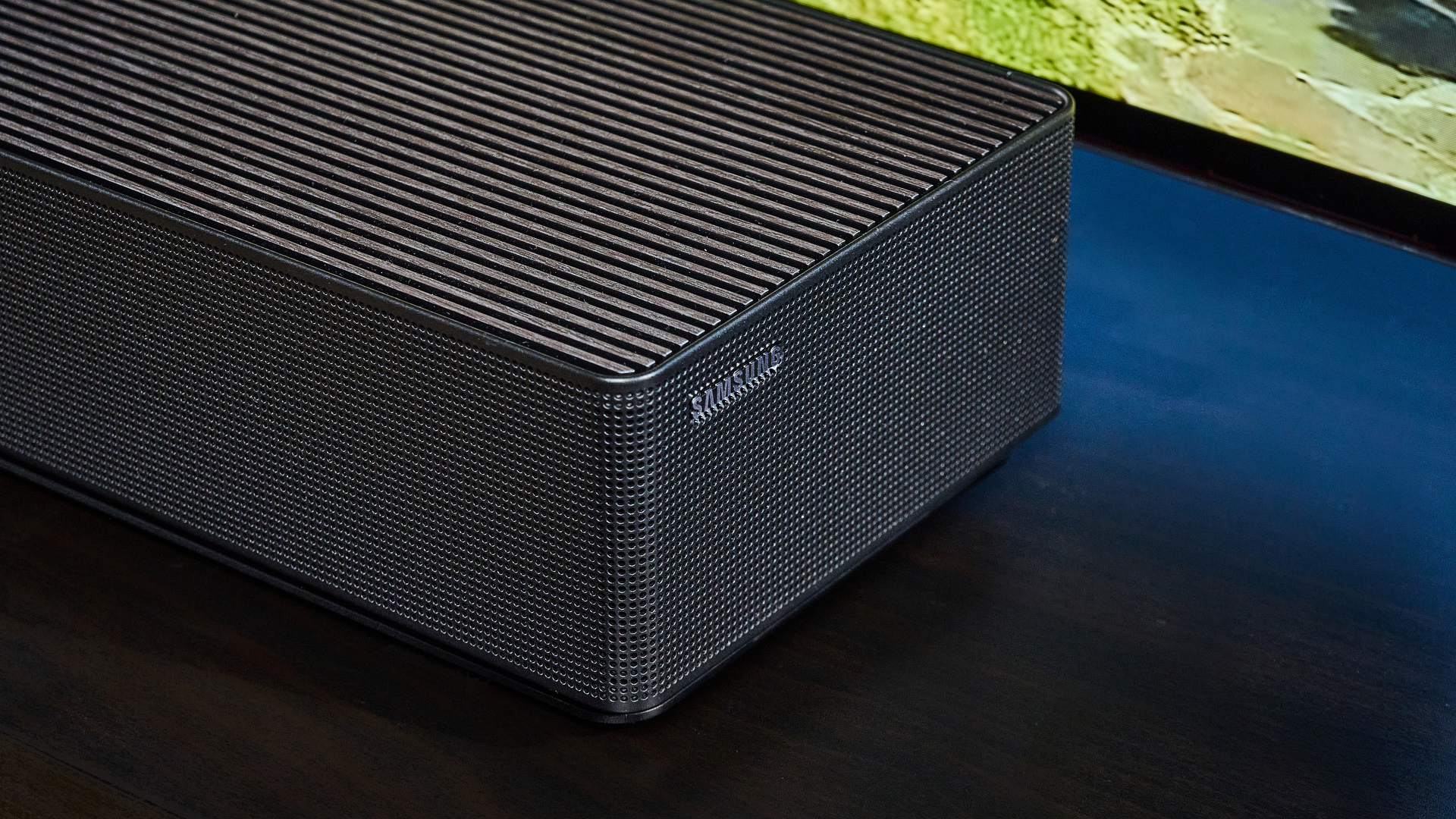 the samsung qs90h soundbar in a living room set with a tv and photographed with the blue tom's guide background