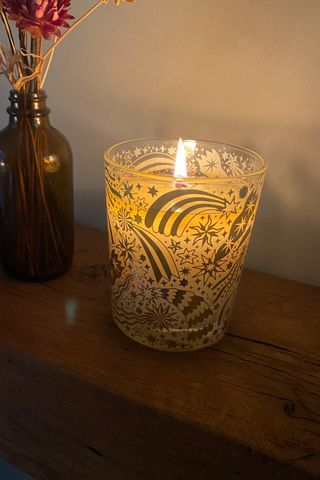 The Space NK Shimmering Spice Candle lit while sitting on a wooden surface