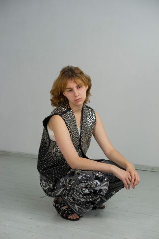 Portrait of woman crouching in Gucci studded waistcoat and sequin trousers