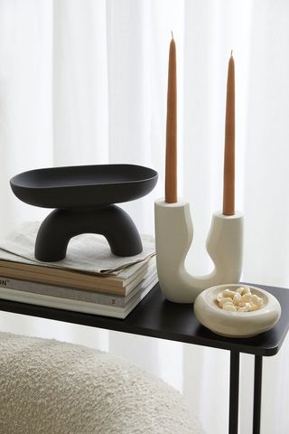 dual height candlestick holding two candles on a side table with other stoneware accessories around