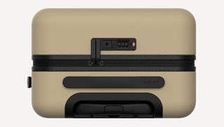 A top-down view of the top of the beige suitcase with its black handle, black carry handle, black zip locks.