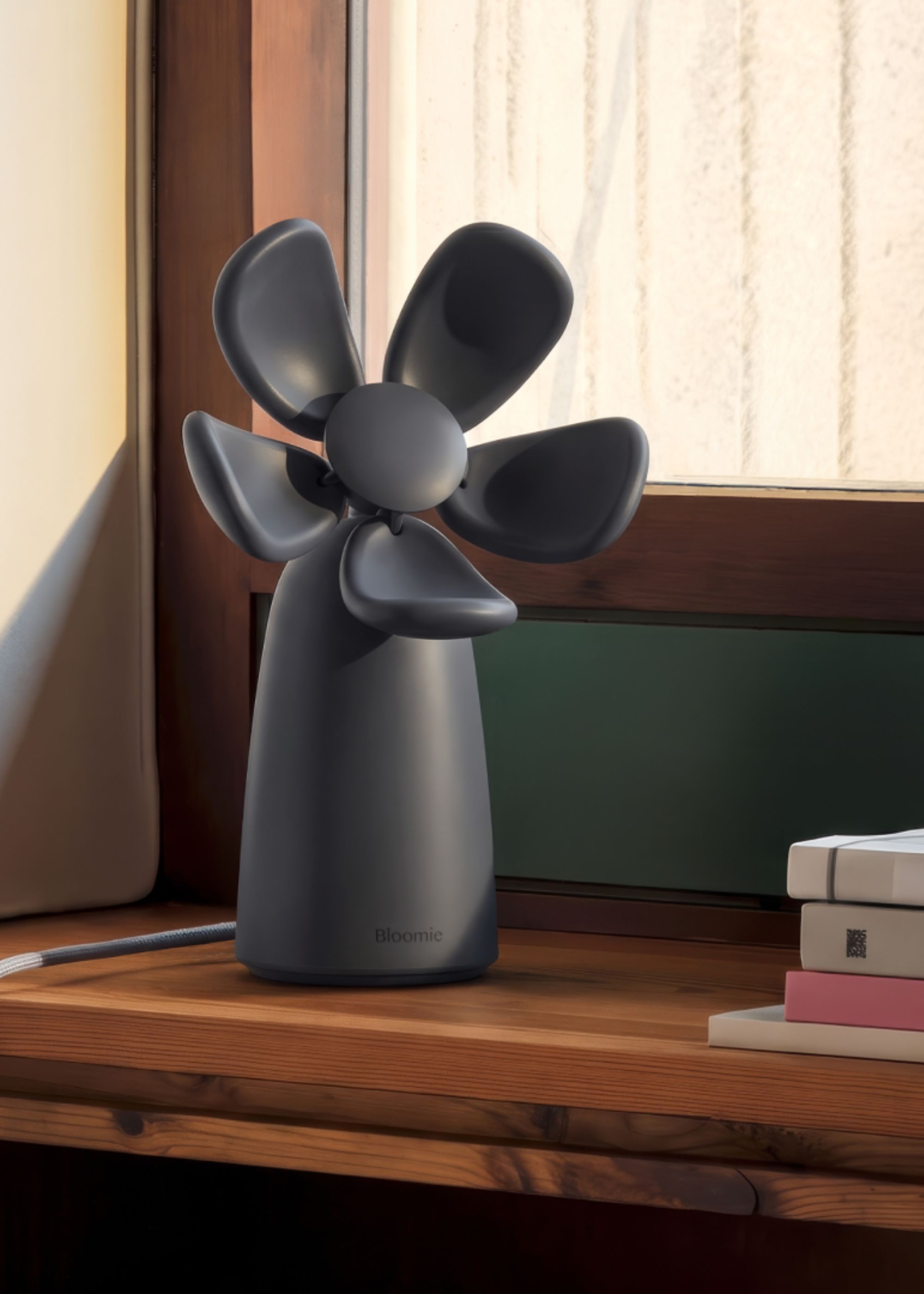 A dark indigo flower-shaped air quality checker from Bloomie on a windowsill beside a stack of books