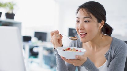 Women eats breakfast out of a cereal bowl and looks happy