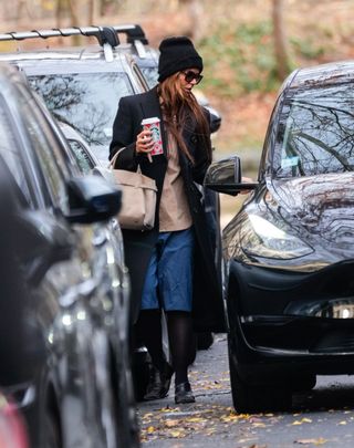 A photo of Katie Holmes topping off her look with a tan button-down shirt, black beanie, and a taupe suede tote bag.