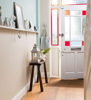 narrow hallway with shelf and front door with red stained glass