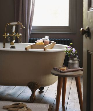 A wooden floored bathroom with free standing tub and wooden stiil, wooden bathroom accessories on a bath tray