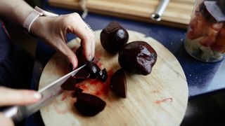 Close-up of woman's hands slicing boiled beets on wooden cutting board with a knife at home kitchen.