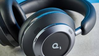 the soundcore space one pro headphones; a close up photograph of a pair of black over-ear headphones with cushioned cups and a soft headband, photographed in front of a blue background, with a reflection of blue on the cups