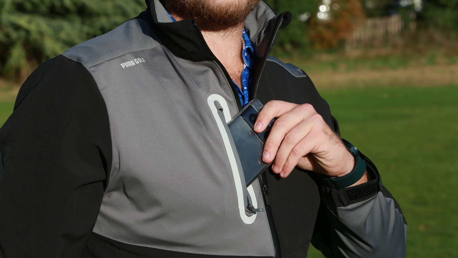 A golfer puts a phone in his Puma Nordic DWR Golf Jacket pocket