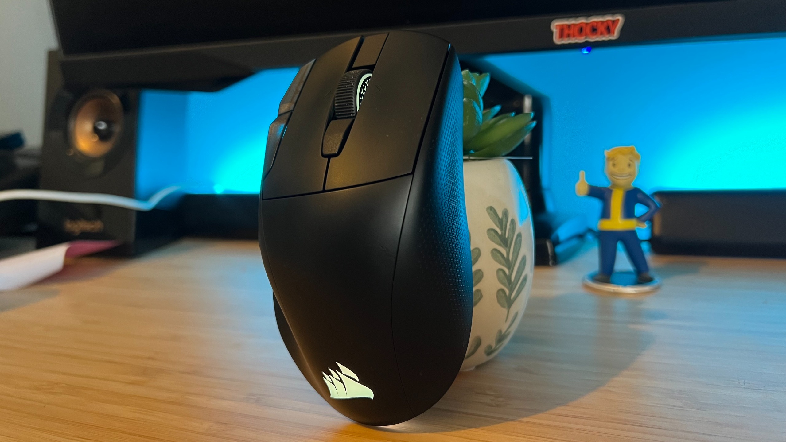 Corsair Nightsword V2 Wireless gaming mouse standing upright on a wooden desk with blue backlighting