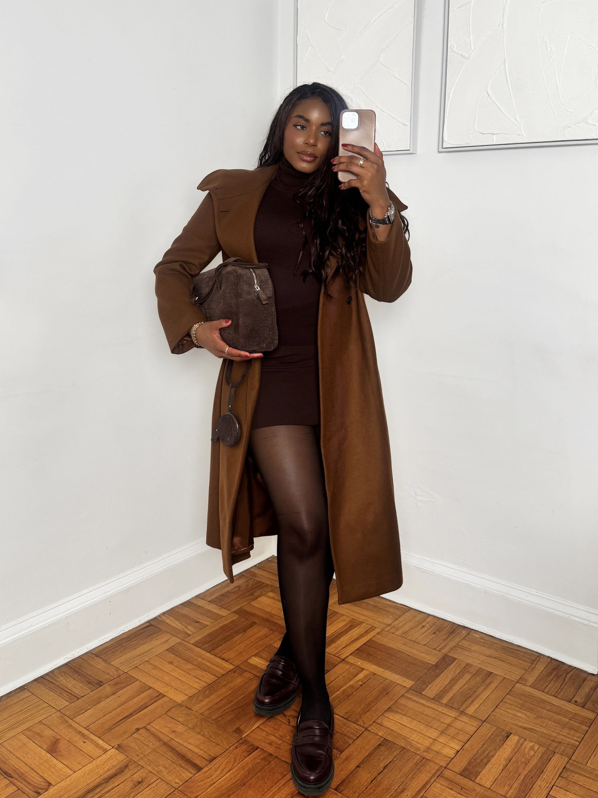 fashion and beauty influencer Kaye Bassey poses in a winter 2026 outfit formula with a brown coat, brown turtleneck top, brown skirt, tights, and brown loafers