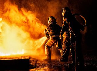 Firefighters using a hose and water to fight a fire.