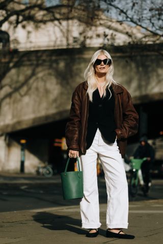 woman wearing leather jacket, black shirt, white pants, and ballet flats