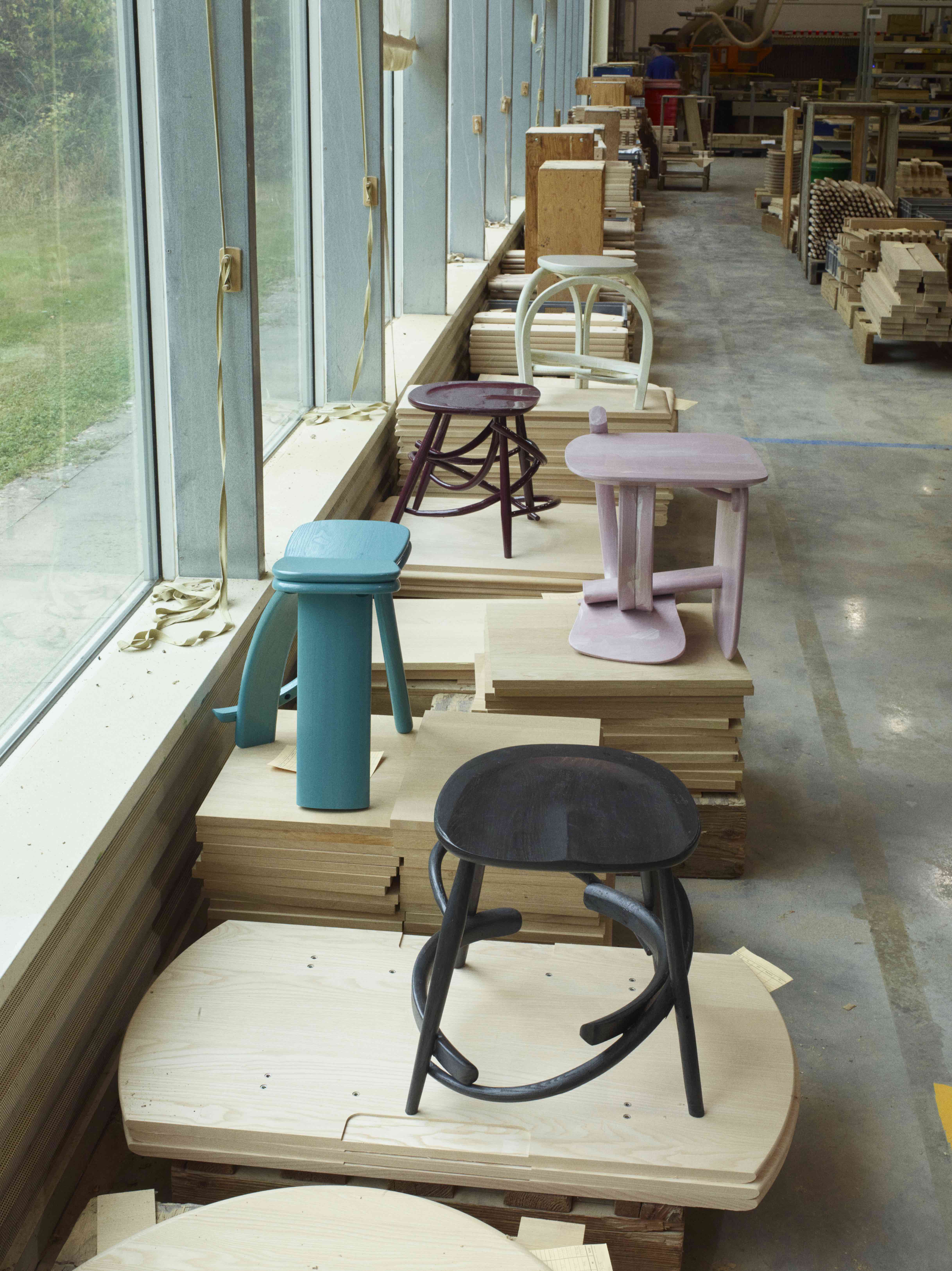 wooden chairs and stools displayed on stacked panels of wood on a factory floor