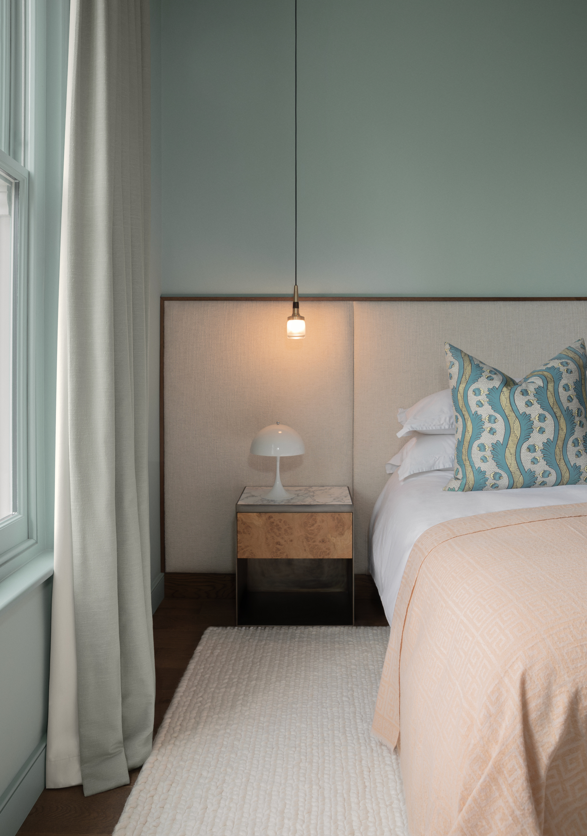 A modern bedroom with the walls painted in an icy blue. The bed has peach bedding with a beige extended headboard.