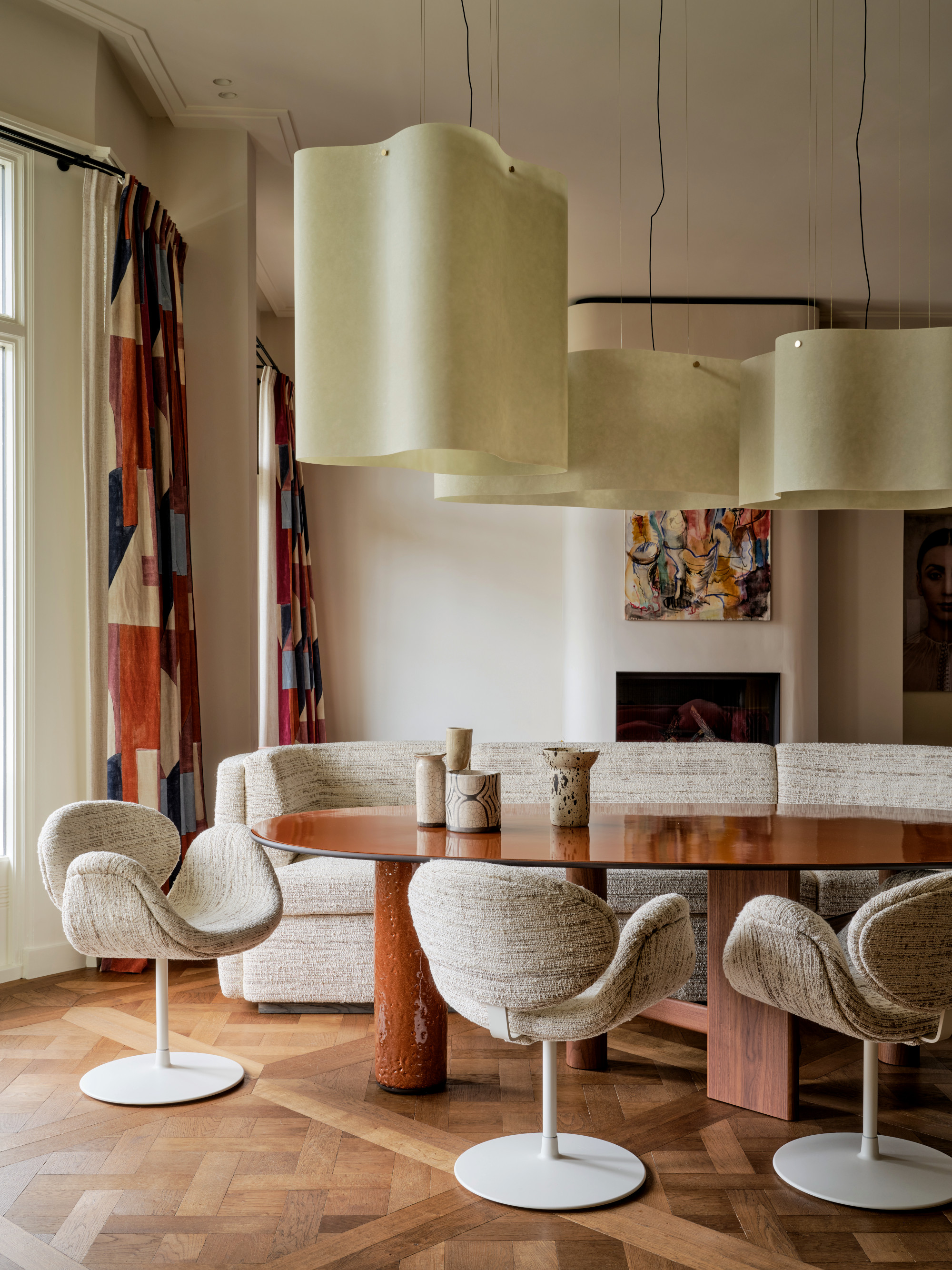 Dining room with sofa and armchair seating, wood oval table, oversized pendants and Versailles style wooden parquet floor