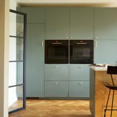 A kitchen with sage green cupboards and two built-in electric ovens