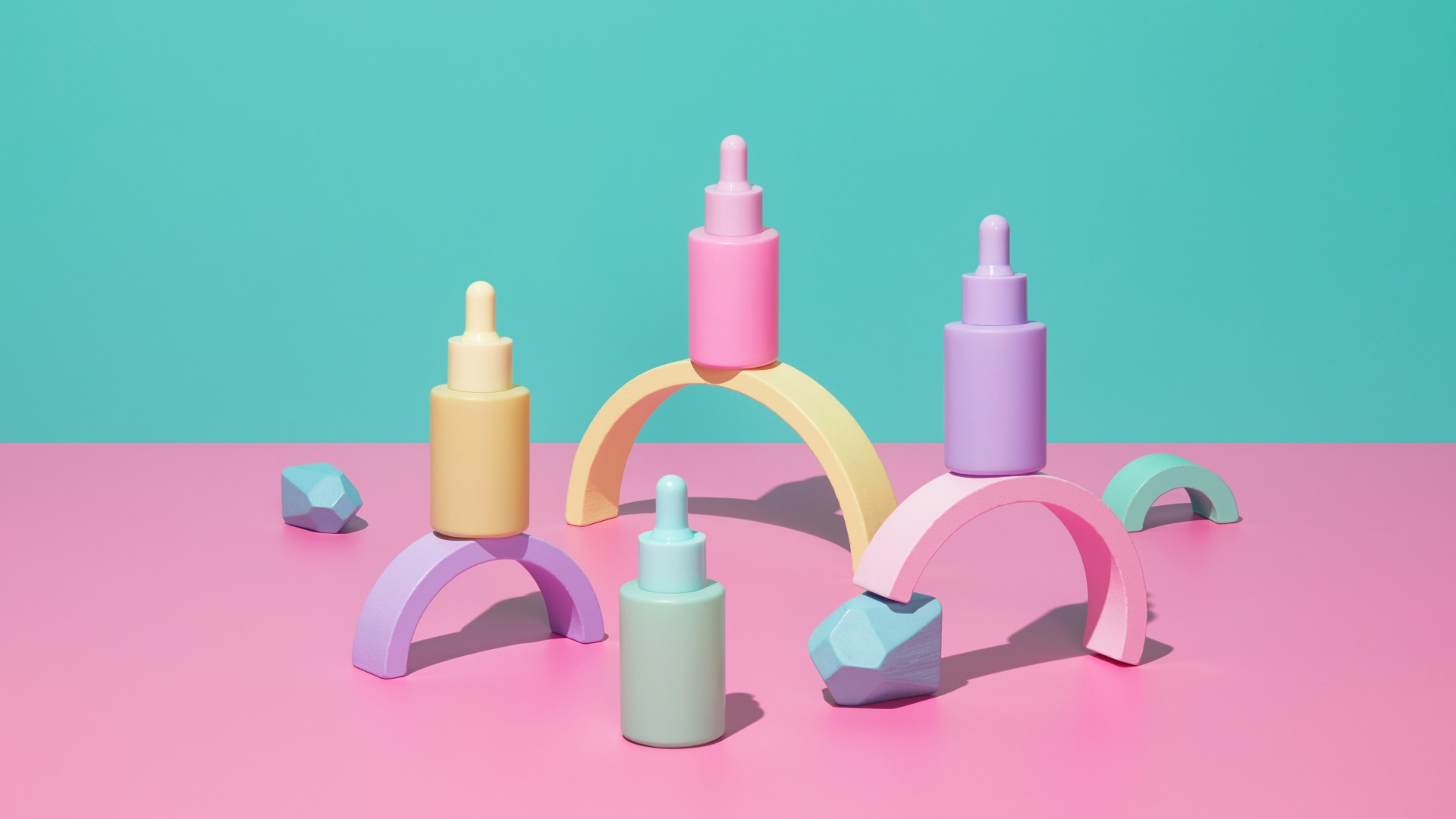 Pastel colorful cosmetics bottles on pink table with abstract geometric figures on turquoise mint green background