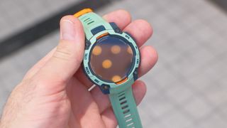 Close up of Garmin Instinct 3 GPS smartwatch in Neotropic/Twilight with a grey and orange case and sea foam green strap