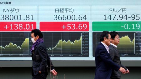 Pedestrians walk past a board with Japanese stocks