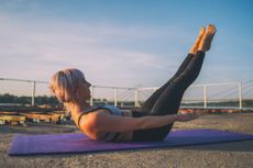 A woman performing the Pilates 100 exercise on a yoga mat outdoors