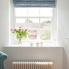 White radiator below a window sill in a white room, with a vase of flowers on the window sill