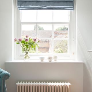 White radiator below a window sill in a white room, with a vase of flowers on the window sill